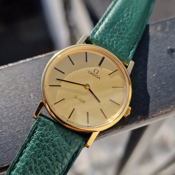 Gold watch with green leather strap on a blurred background