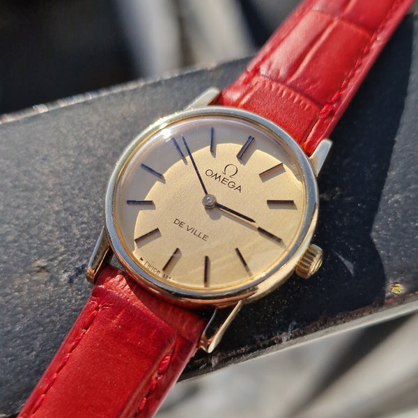 Wristwatch with red strap and gold case on a blurred background