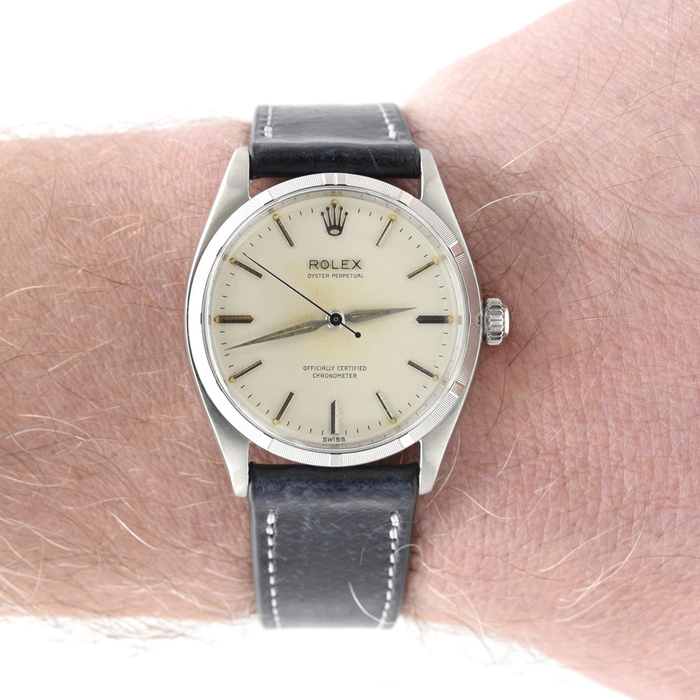 A Rolex 6465 watch with a silver-toned case, cream-colored dial, and a dark gray leather strap, shown worn on a person's wrist.