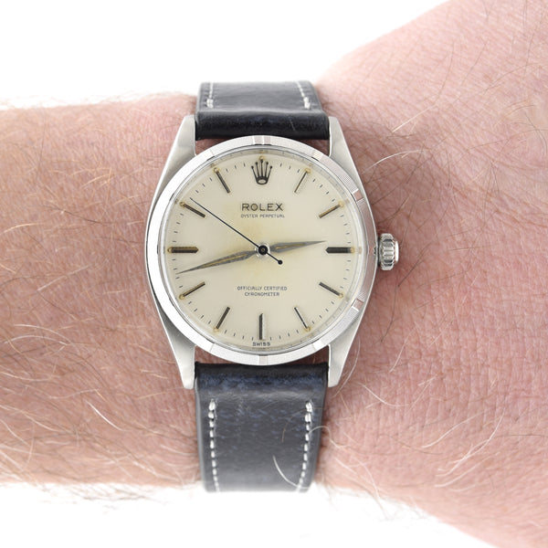 A Rolex 6465 watch with a silver-toned case, cream-colored dial, and a dark gray leather strap, shown worn on a person's wrist.