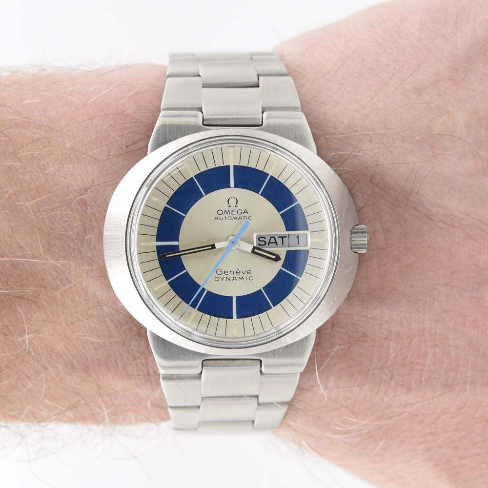 Omega Geneve Automatic wristwatch with a stainless steel link bracelet, featuring a blue and silver dial with a day-date window, shown worn on a wrist.