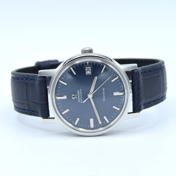 Omega x Swatch Calibre 1 watch with a dark blue dial, silver stainless steel case, and a dark blue leather strap with blue stitching, shown on a light gray background.