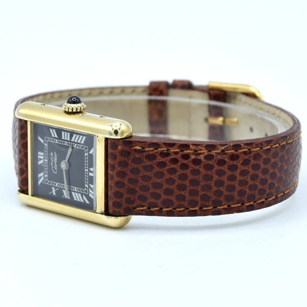 A Cartier Tank watch with a brown textured alligator leather strap and a gold-tone case with a black dial and Roman numerals.