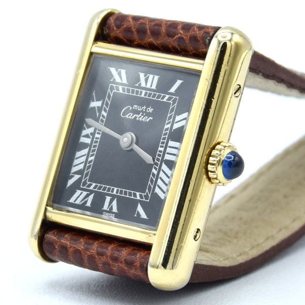 A Cartier watch with a gold-tone rectangular case, black dial with Roman numerals, and a brown textured leather strap, photographed on a white background.