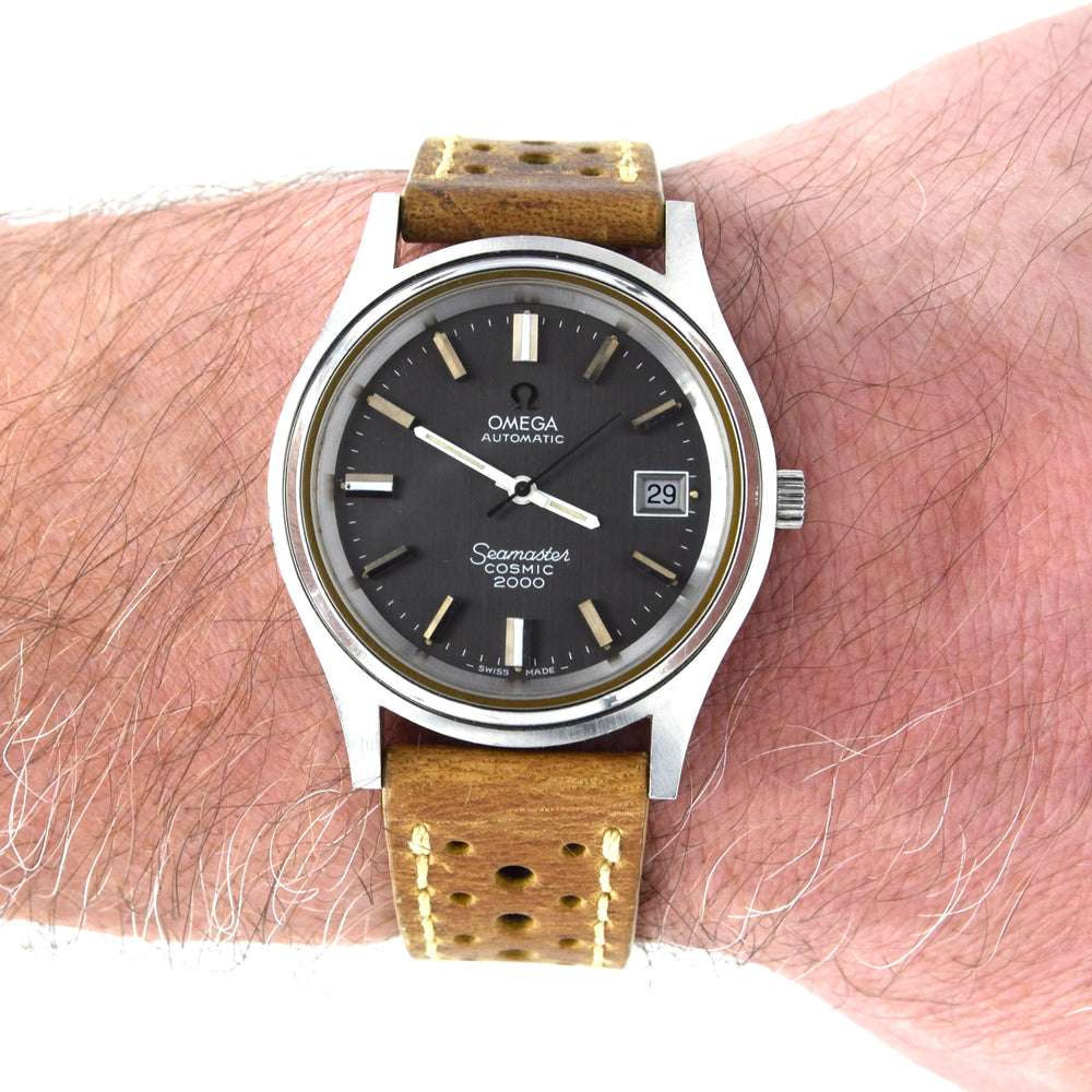 A vintage Omega Seamaster 2000 watch with a black dial and brown perforated leather strap, shown worn on a person's wrist against a white background.