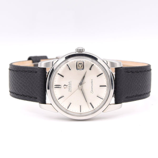 A vintage Omega Seamaster wristwatch with a silver-tone stainless steel case, a cream-colored dial, and a black textured leather strap, shown against a plain white background.