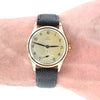 Vintage Omega watch with a gold case and gray strap on a wrist.
