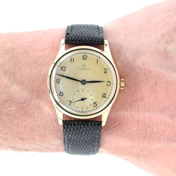 Vintage Omega watch with a gold case and gray strap on a wrist.