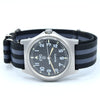 A vintage-style wristwatch with a black dial, silver-tone metal case, and a black and gray striped nylon strap, shown on a plain white background.