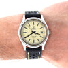 A wristwatch with a cream-colored dial and a black perforated leather strap, shown worn on a person's wrist. The watch has a silver-tone case and black indices, with the Omega brand name visible on the dial.