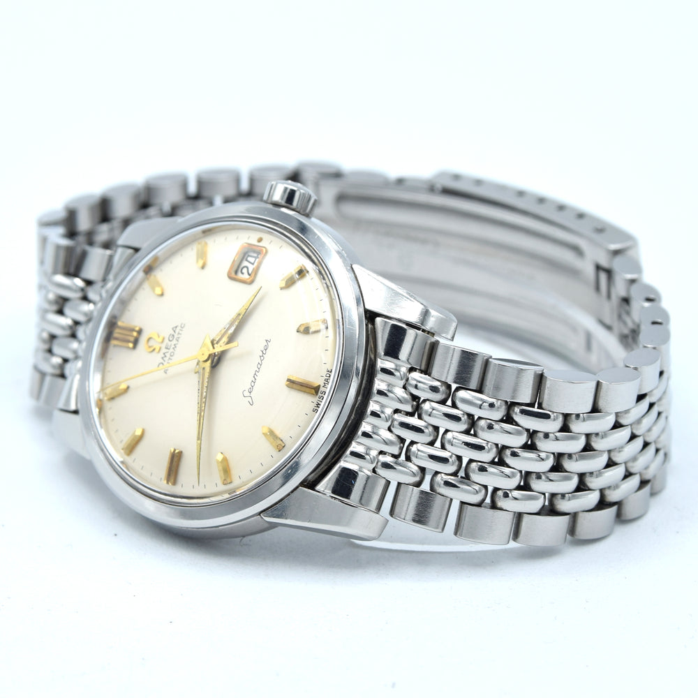 A vintage Omega watch with a silver stainless steel link bracelet and a cream-colored dial featuring gold-tone hands and hour markers.