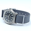 A wristwatch with a dark gray fabric NATO-style strap, a brushed stainless steel case, and a black dial featuring white Arabic numerals and gold-tone hands.