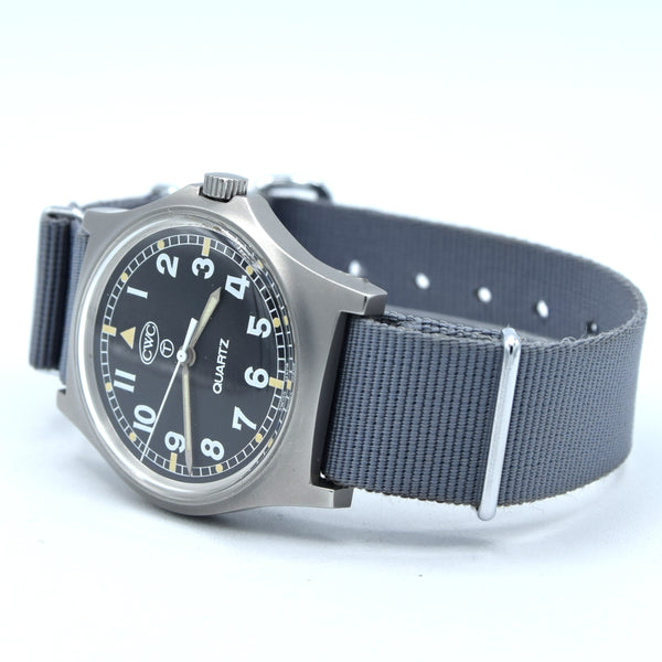 A wristwatch with a dark gray fabric NATO-style strap, a brushed stainless steel case, and a black dial featuring white Arabic numerals and gold-tone hands.
