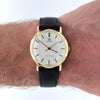 An Omega watch with a gold case, white dial, and black leather strap worn on a person's wrist against a white background.