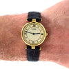 A Cartier watch with a gold case, cream dial, and black leather strap, shown worn on a person's wrist against a white background.