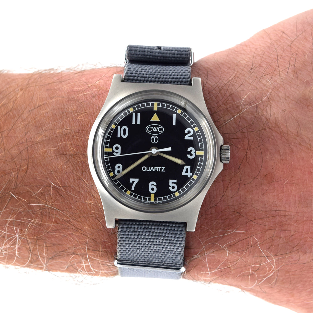 A wristwatch with a black dial, silver-toned metal case, and a dark gray fabric strap, shown worn on a person's wrist against a white background.