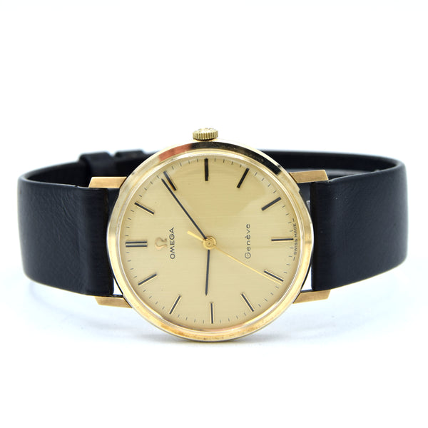 Omega Geneva wristwatch with a round gold-tone case, gold dial, and black leather strap, photographed on a white background.