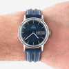 Omega Automatic wristwatch with a dark blue dial and blue leather strap, shown worn on a person's wrist against a white background.