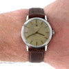 A vintage Omega Seamaster wristwatch with a brown textured leather strap and a champagne-gold dial, shown worn on a person's wrist against a white background.