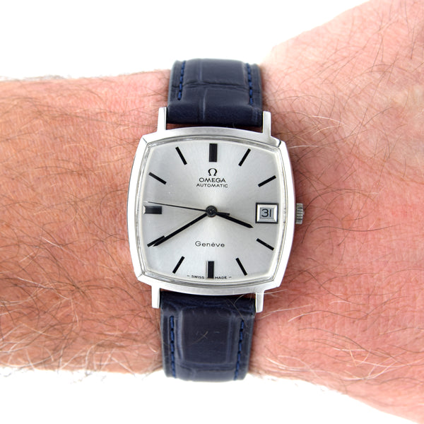 A vintage Omega Automatic watch with a silver dial and a dark blue leather strap, shown worn on a person's wrist against a white background.