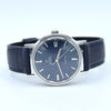 Omega x Swatch Calibre 1 watch with a dark blue dial, silver stainless steel case, and a dark blue leather strap with blue stitching, shown on a light gray background.