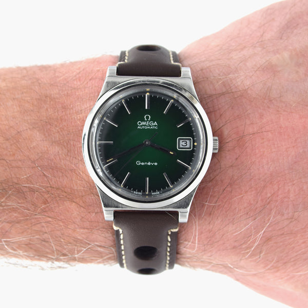 An Omega Automatic wristwatch with a dark green dial and a dark brown leather strap, shown worn on a person's wrist against a white background.