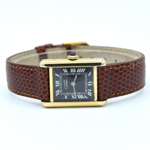 A Cartier Tank watch with a brown textured leather strap, gold-tone case, and a black dial with Roman numerals, shown on a white background.
