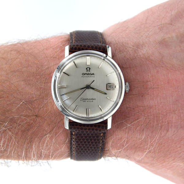 A vintage Omega De Ville watch with a silver dial and brown textured leather strap, shown worn on a person's wrist against a white background.